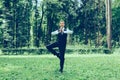 Attractive young man in a suit does yoga tree pose in a park Royalty Free Stock Photo