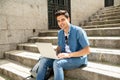 Attractive young modern man working with computer in the city on outside stairs Royalty Free Stock Photo