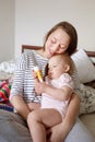 Attractive young mother sitting on bed holding her sweet little baby on her hands Royalty Free Stock Photo