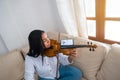 An attractive young musician plays the violin sitting on the sofa. The girl is practicing playing a musical instrument at home