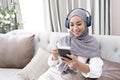 Attractive young Muslim woman sitting in living room, using smartphone and laptop computer. cropped image Royalty Free Stock Photo