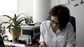 Attractive young office woman in white shirt working on the business papers, signing documents near green plant and Royalty Free Stock Photo