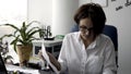 Attractive young office woman in white shirt working on the business papers, signing documents near green plant and Royalty Free Stock Photo