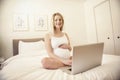 Attractive young pregnant woman with laptop on bed Royalty Free Stock Photo