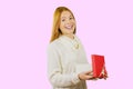 Attractive young red-haired girl, with an open box with a gift, smiles with an open mouth and looks into the camera
