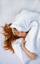 Attractive, young, red-haired woman, hair wild on the sheets, face half under the pillow lying in fresh soft white sheets Royalty Free Stock Photo