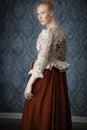 Red-haired 18th century woman standing in front of baroque wall paper Royalty Free Stock Photo