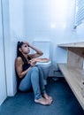 Attractive young and sad bulimic young woman feeling guilty and sick eating while sitting on the floor next to the toilet in Royalty Free Stock Photo
