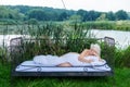 Attractive, young, sexy, blonde woman lying naked covered with white duvet in bed sleeping in the nature in front of a lake Royalty Free Stock Photo