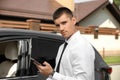 Attractive young with smartphone near luxury car outdoors