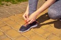 Attractive young sports woman sitting on knee and tying shoe laces on sneakers while having rest during morning jog outdoors. Royalty Free Stock Photo