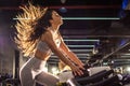 Attractive young sportswoman with long hair in the air riding stationary bike during cycling training in gym. Royalty Free Stock Photo