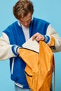 an attractive young student stands with an orange backpack in his hands and looking inside takes out his notebook Royalty Free Stock Photo