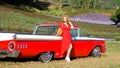 Attractive young stylish woman in dress standing near red retro sports car on country road on sunny summer day. Vintage Royalty Free Stock Photo