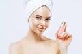 Attractive young woman applies parfum, enjoys pleasant scent, stands with naked shoulders, has natural makeup, healthy skin,