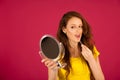 Attractive young woman applying lip gloss looking in mirror over pink background Royalty Free Stock Photo