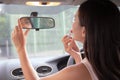 Attractive young woman applying lipstick looking at mirror in car..Girl adjusts her makeup putting lipstick while sitting at the Royalty Free Stock Photo