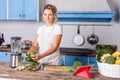 Attractive young woman in apron cooking green salad, preparing vegetarian food in modern kitchen Royalty Free Stock Photo