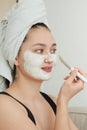 An Asian woman applies a white clay cosmetic mask to her face. Beautiful woman with a towel on her head cares for her Royalty Free Stock Photo