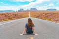 Attractive young woman from back view sitting in the middle of American straight road in the desert. Royalty Free Stock Photo