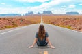 Attractive young woman from back view sitting in the middle of American straight road in the desert. Royalty Free Stock Photo