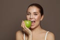 Attractive young woman biting green apple and smiling on brown background Royalty Free Stock Photo