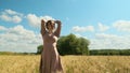 attractive young woman in brown dress walks along yellow field against blue sky with clouds. beautiful beauty lady spin Royalty Free Stock Photo