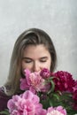 Attractive young woman with brown hair enjoys smell of peonies. Girl with natural beauty with bouquet of peonies. Vertical frame