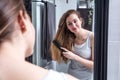 Attractive young woman brushing long hair in front of mirror Royalty Free Stock Photo