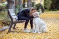 Attractive young woman caring and playing with her beautiful golden retriever dog while sitting on bench in the park Royalty Free Stock Photo