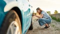 Attractive young woman checking air pressure of car tire on local road side while traveling Royalty Free Stock Photo