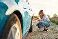 Attractive young woman checking air pressure of car tire on local road side while traveling, Girl having troubles with Royalty Free Stock Photo