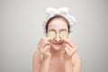 Attractive young woman covering her eyes with cucumbers on a blue background. Clay mask Royalty Free Stock Photo