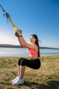 Attractive young  woman  doing TRX training outdoors near the lake at daytime. Healthy lifestyle Royalty Free Stock Photo