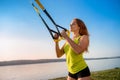 Attractive young  woman  doing TRX training outdoors near the lake at daytime. Healthy lifestyle Royalty Free Stock Photo