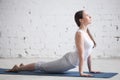 Attractive young woman doing upward facing dog pose in white loft