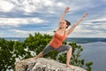 An attractive young woman doing a yoga pose for balance on the rock.