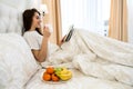 Attractive young woman drinking coffee with fruit in the morning reads her notebook in bed. Weekend concept Royalty Free Stock Photo