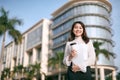 Attractive young woman drinking coffee and reading her touchscreen tablet while standing outside a commercial building Royalty Free Stock Photo