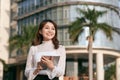 Attractive young woman drinking coffee and reading her touchscreen tablet while standing outside a commercial building Royalty Free Stock Photo