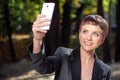 Attractive young woman in formalwear taking photo with her cellphone in park Royalty Free Stock Photo