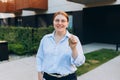 Attractive young woman in glasses showing key while standing outdoor against new house. Real estate agent holding key on Royalty Free Stock Photo