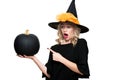 Attractive young woman in Halloween Witch costume holding large black pumpkin and pointing with a finger at it.