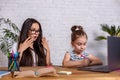 Attractive young woman and her little cute daughter are sitting at the table and having fun while doing homework Royalty Free Stock Photo