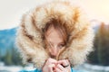 Attractive young woman hiding under her big fur hood in winter.