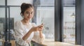 Attractive young woman holding mobile phone and smiling to camera while sitting in coffee shop Royalty Free Stock Photo