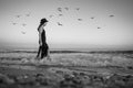 Attractive young woman in long dress and hat walking thoughtfully into raging sea