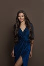 Attractive young woman with long healthy hair in blue shiny evening gown standing on brown background Royalty Free Stock Photo