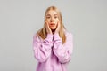 Attractive young woman, looking worried and shocked, terrified of something, wears violet hoody, stands against grey background