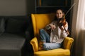 Attractive young woman musician plays the violin sitting on soft chair Royalty Free Stock Photo